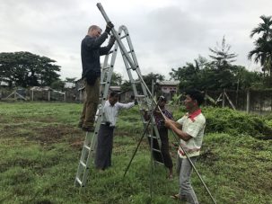 Keith sliding our homemade post pounder along a diagonal rod to drive it in while Zaw Min steadies it.