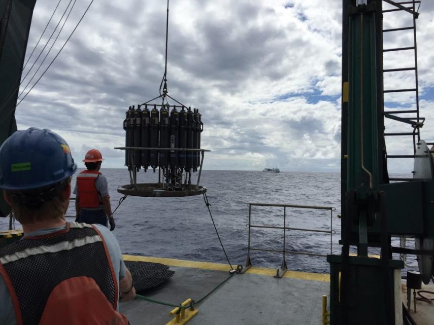 The water sampling device, called a rosette, is lowered off the back of the ship into the North Pacific. Each of the 24 grey bottles can hold 12 L of seawater that was used for sampling.The ship in the distance is the R/V Ka’imikai-o-kanaloa, the sister ship of this expedition. Photo: Kyle Frischkorn water sampling device is lowered off the ship into the ocean